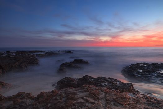 Long exposure of sunset over rocks, giving a mist like effect over ocean in Laguna Beach, California, United States