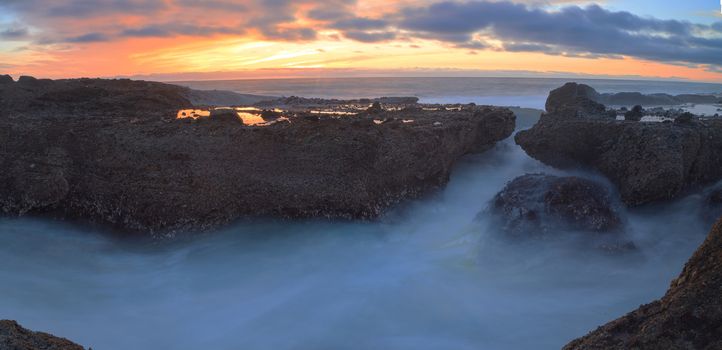 Long exposure of sunset over rocks, giving a mist like effect over ocean in Laguna Beach, California, United States