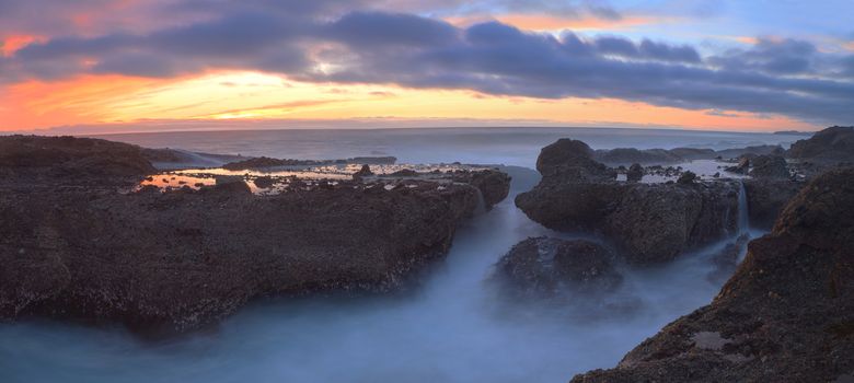 Long exposure of sunset over rocks, giving a mist like effect over ocean in Laguna Beach, California, United States