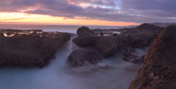 Long exposure of sunset over rocks, giving a mist like effect over ocean in Laguna Beach, California, United States