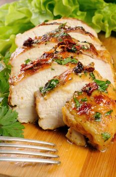  Slices of roasted chicken breast on a wooden board with fresh herbs