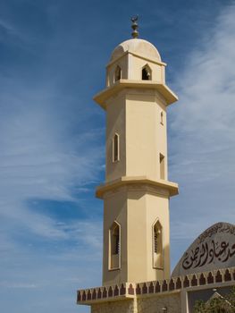 Light yellow color of the facade of a mosque in Egypt. Details of the tower. Blue sky with intense white clouds.