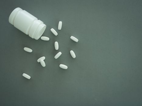 Pills spilling out of pill bottle on gray background. Top view