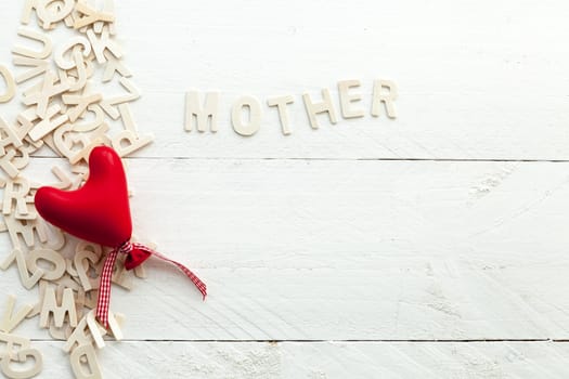 Image related to the celebration of Mother's Day on white wooden background, wooden letters and a red heart view from above