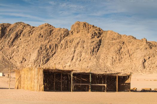 Rocky mountains in the sand color in the desert in Egypt. Bedouin building for the guests. Cloudy sky.