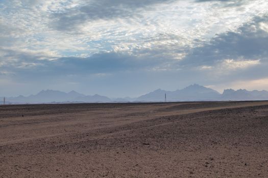 Plane sandy terrain in the desert in Egypt, close to the coast and city Hurghada. Line of mountains in the background. Intense clouds before the sunset.