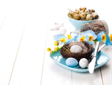 table decoration with easter eggs nest on plate, on white wooden background