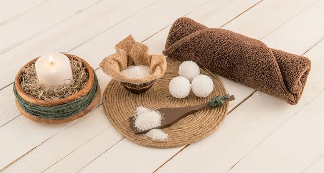 Spa scene with bath bombs, mineral bath salts, and candle on rustic white planks
