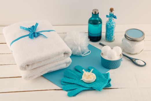 Pampering bath items: bath bombs, mineral bath salts, bath beads, bath oil, pouf, soap and spa towel, on rustic white wood planks