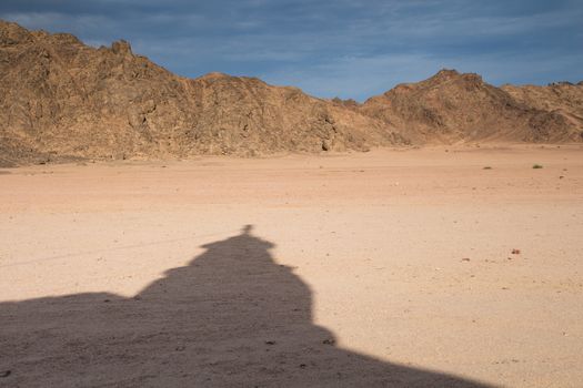 Shadow of the tower of a small bedouin mosque in the desert close to Hurghada in Egypt. Mountains and cloudy sky in the background.