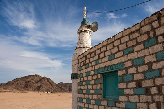 Tower of a small bedouin mosque in the desert close to Hurghada in Egypt. Mountains in the background. Cloudy sky.