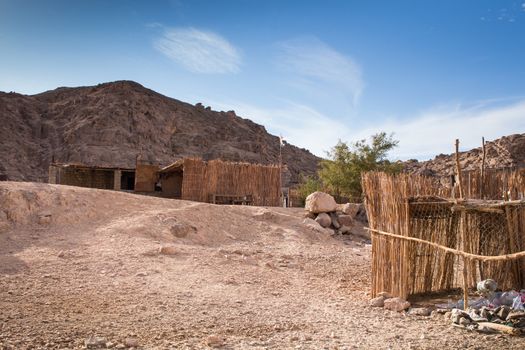 Bedouin village in the desert in Egypt, their buildings and fence. Rocky mountain in the background. Intense cloudy sky.