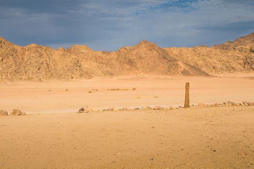 Valley between the rocky mountains in egyptian desert. Golden color of the sand and rocks thanks to the late afternoon sunlight. Cloudy sky.