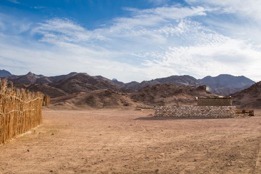 Valley between the rocky mountains in egyptian desert. Place of bedouin village, building visible. Intense cloudy sky.