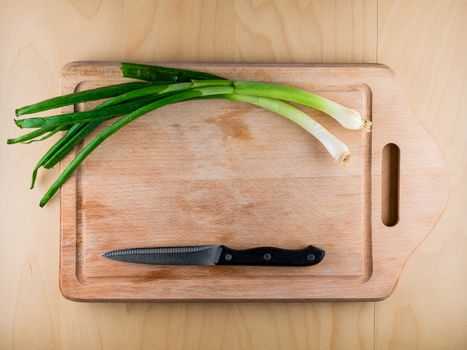 Bunching onion on the wooden board with a knife, from the top view, food preparation in the kitchen, copy space in the middle