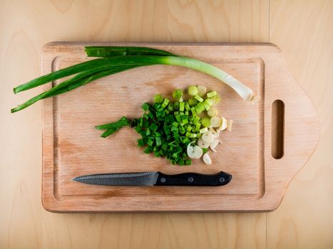 Pieces of bunching onion on the wooden board with a knife, from the top view, food preparation in the kitchen
