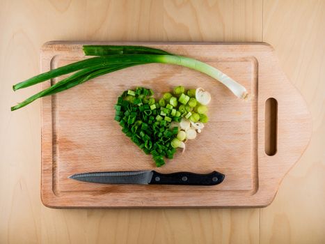 Heart shaped pile of bunching onion on the wooden board with a knife, from the top view, healthy life style