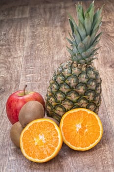 Orange oranges, pineapple, kiwi and apple on a brown wooden background