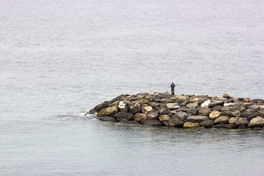 Fisher man with fishing rod on the stone groyne