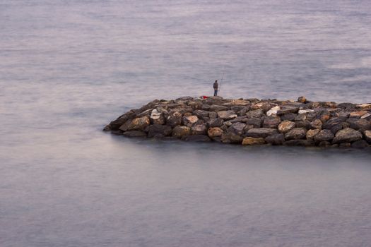 Fisher man with fishing rod on the stone groyne at sunset