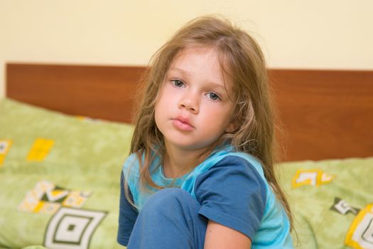 Funny five-year girl waking up sitting on the bed in pajamas