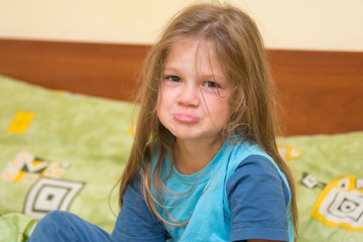 Funny five-year girl waking up sitting on the bed in pajamas