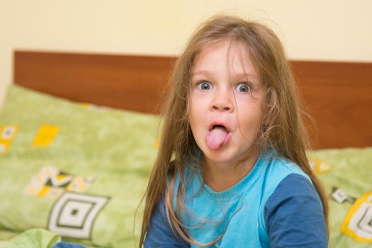 Funny five-year girl waking up sitting on the bed in pajamas