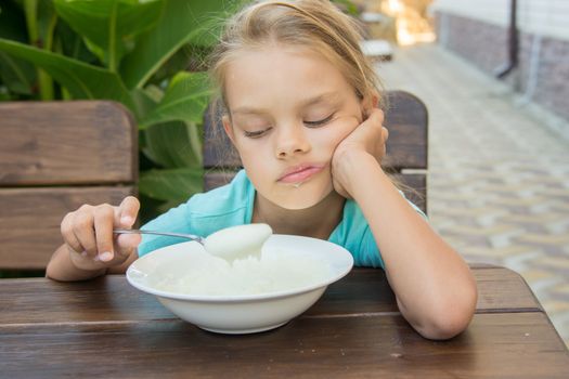 Six-year girl sitting at a table with a sour face and did not want to eat porridge for breakfast