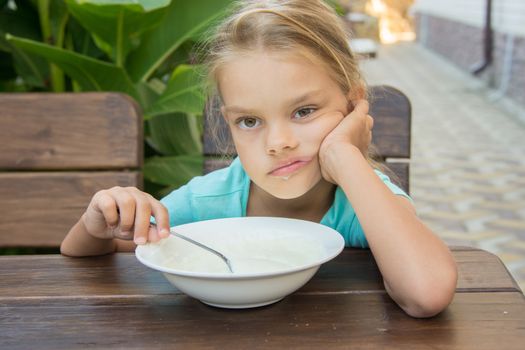 Six-year girl sitting at a table with a sour face and did not want to eat porridge for breakfast
