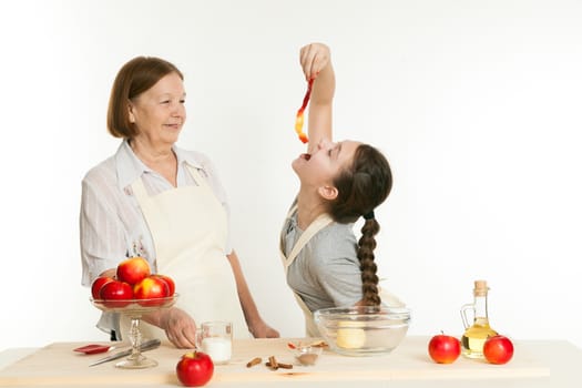 the grandmother looks as the granddaughter eats a peel from apple