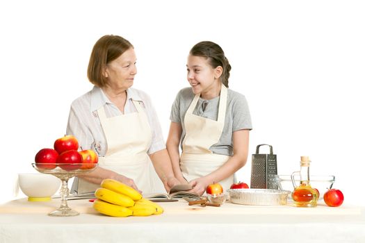 the grandmother and the granddaughter read the recipe-book before cooking of food and smile each other