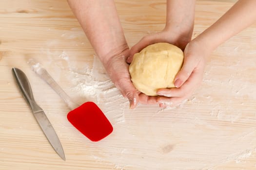 hands of the grandmother and hand of the granddaughter hold dough on a kitchen table