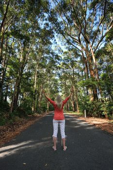 Female standing among the tall gum trees on a remote country road with arms outstretched.