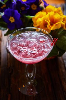 cosmopolitan cocktail garnished with ice on wooden table and flowers background