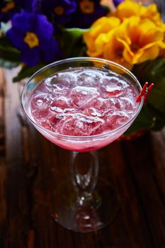 cosmopolitan cocktail garnished with ice on wooden table and flowers background