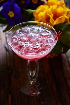 cosmopolitan cocktail garnished with ice on wooden table and flowers background