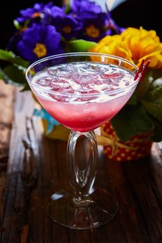 cosmopolitan cocktail garnished with ice on wooden table and flowers background