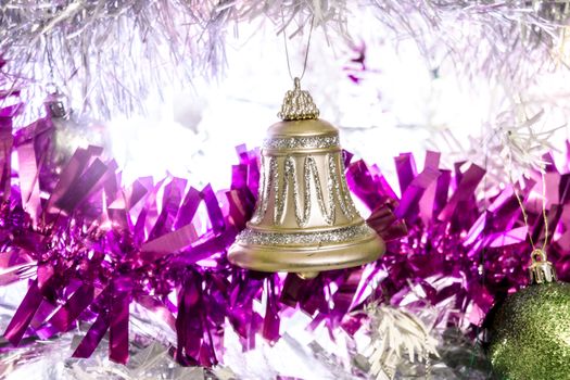 A gold glittery bell on w white christmas tree covered in purple tinsil