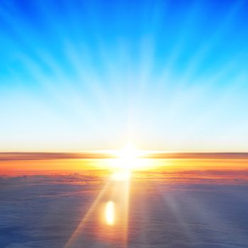 View on sun, sunset, blue sky, and ocean of clouds from airplane window.