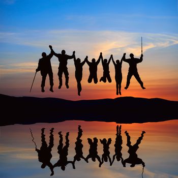 Silhouette of jumping friends on the beach with reflection against sunset