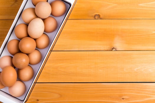 Storage container of healthy brown farm eggs on a wooden table with copy space viewed from above