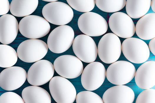 Background pattern of multiple small white sugar-coated Easter eggs on a blue picnic table viewed as a layer from above