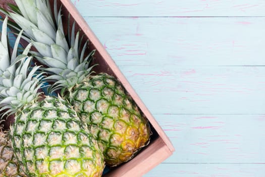 Fresh pineapples in a wooden crate displayed at an angle on a blue painted wooden table with copy space, overhead view