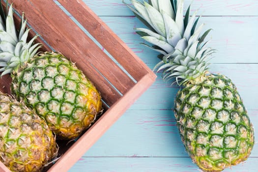 Three fresh pineapples, two in a wooden crate and one alongside on a blue wooden table lying on their sides viewed close up from above