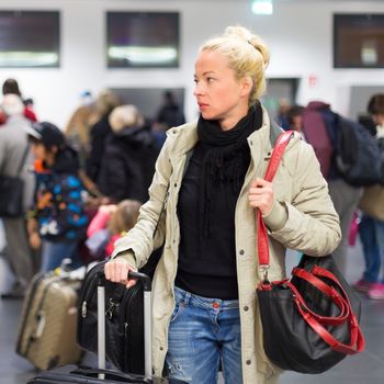 Casually dressed young female traveller waiting in airport arrival terminal hall,  collecting her laggage . Blured background. Can also be used as railway, metro, bus station.