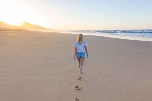 Woman walking on sandy beach in sunset leaving footprints in the sand. Beach, travel, concept. Copy space.