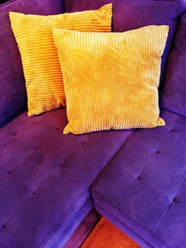 Vibrant purple sofa decorated with two orange cushions.