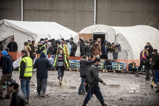 FRANCE, Grande-Synthe: Migrants gather outside tents at the new camp at Grande Synthe on March 7, 2016.The new camp features make shift shelters to provide more protection from the elements. Also available are better sanitation measures including showers and toilets.   