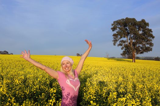 Happy smiling exuberant woman in a field of golden canola with arms raised above her head in the early morning sunshine