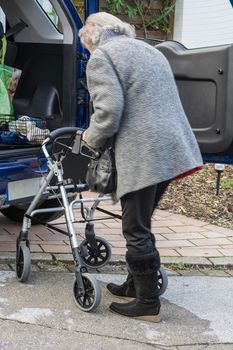 Senior lady standing with a Walking frame on the car.